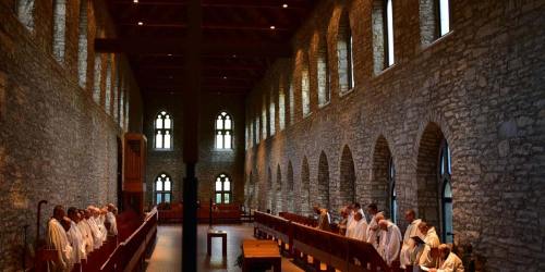 A serene stone chapel interior with arched windows, featuring individuals in white robes engaged in prayer.