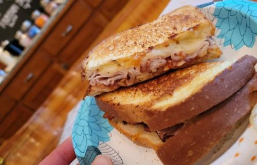 A toasted sandwich with layers of meat and cheese, served on a paper plate with a floral design.