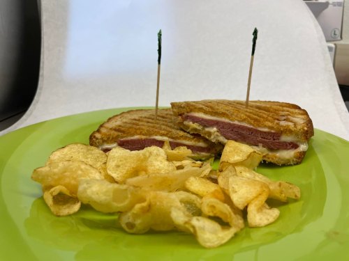 A grilled sandwich with two toothpicks, served on a green plate alongside a pile of potato chips.