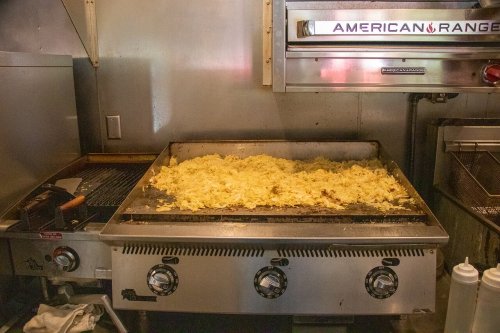 A griddle in a kitchen with a large amount of cooked rice or grains spread across the surface.