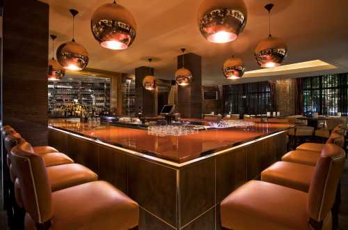 A stylish bar with warm lighting, modern decor, and circular pendant lights, featuring a sleek counter and seating.