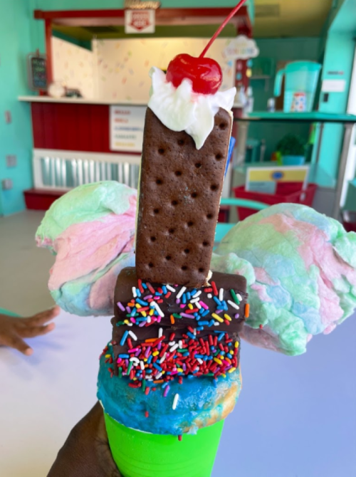 A colorful ice cream treat with cotton candy, sprinkles, and a chocolate wafer topped with a cherry.