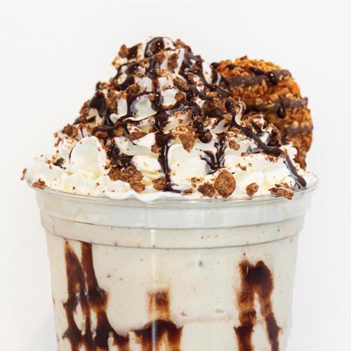 A creamy dessert in a cup topped with whipped cream, chocolate drizzle, cookie crumbles, and a cookie on the side.