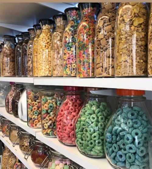 A colorful display of various cereals in glass jars on a shelf, showcasing a variety of shapes and colors.
