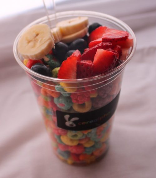 A clear cup filled with colorful cereal, topped with sliced bananas, strawberries, and blueberries.