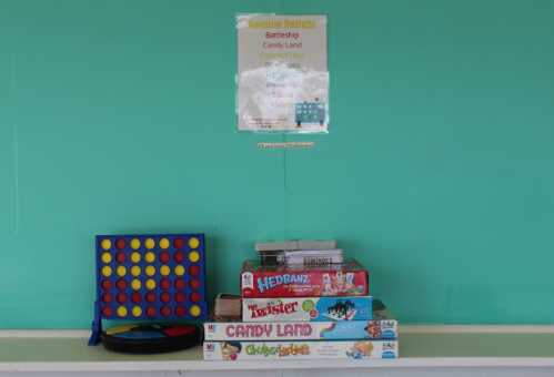 A shelf with board games including Battleship, Candy Land, and Twister, against a teal wall with a sign above.
