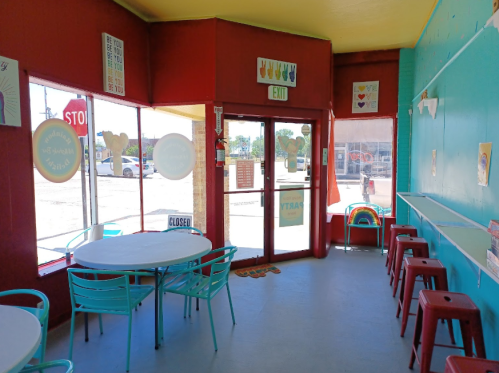 Brightly colored café interior with tables, chairs, and cheerful decor. A "CLOSED" sign is visible on the door.
