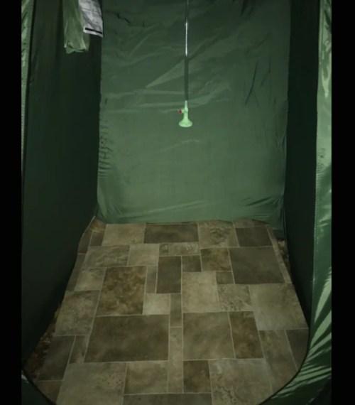 A green tent interior with a tiled floor and a hanging fixture in the center.