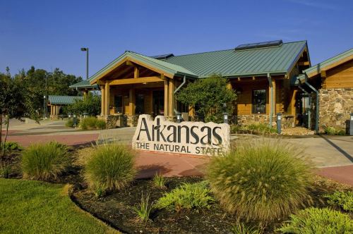 A wooden building with a green metal roof, featuring a stone sign that reads "Arkansas, The Natural State."