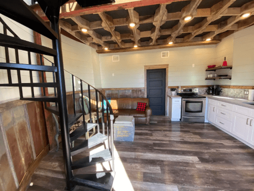 Cozy interior with a spiral staircase, wooden ceiling, and modern kitchen appliances in a well-lit space.