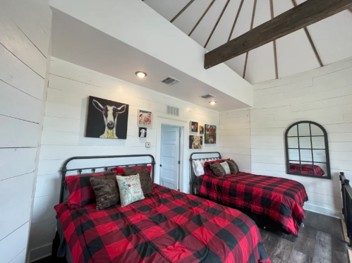 Cozy bedroom with two beds featuring red and black plaid bedding, wooden beams, and wall art.