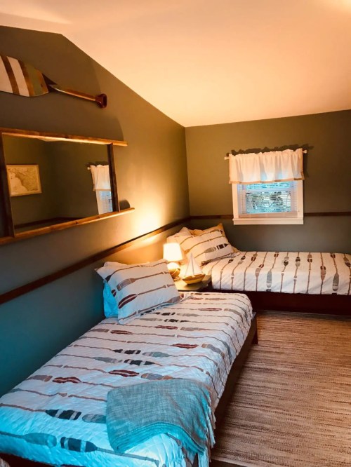 Cozy bedroom with two beds, a mirror, and a warm color scheme, featuring striped bedding and a woven rug.