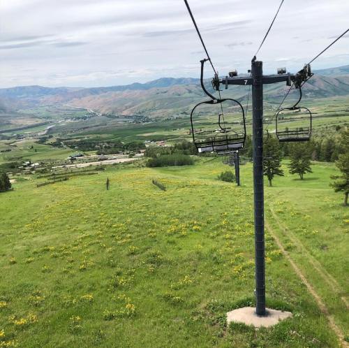 A scenic view from a ski lift overlooking green fields and distant mountains under a cloudy sky.