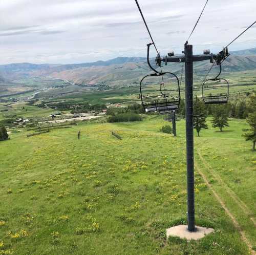 A scenic view from a ski lift overlooking green fields and distant mountains under a cloudy sky.