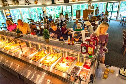 A busy buffet restaurant with diners serving themselves from a variety of food options, surrounded by large windows.