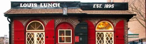 Historic Louis Lunch restaurant exterior, featuring red accents and arched windows, established in 1895.