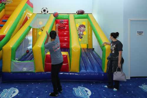 A child throws a ball at a colorful inflatable play structure while an adult watches nearby.