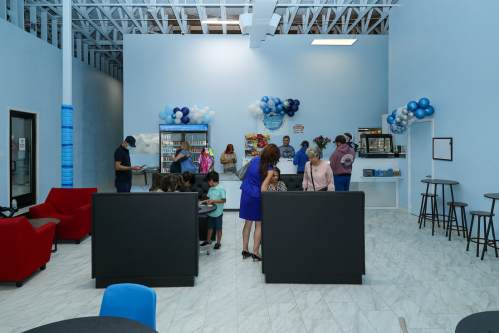 A bright, modern café with people socializing, colorful balloons, and seating areas in a spacious interior.