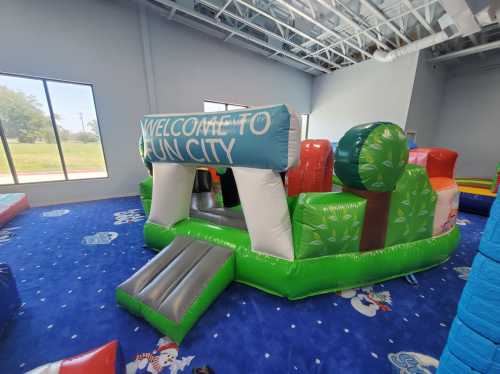 A colorful inflatable play structure with "Welcome to Fun City" sign, set in a spacious indoor play area.