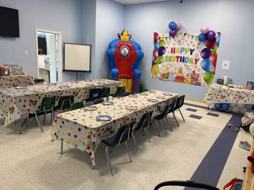 A decorated birthday party room with tables, colorful tablecloths, balloons, and a festive banner.