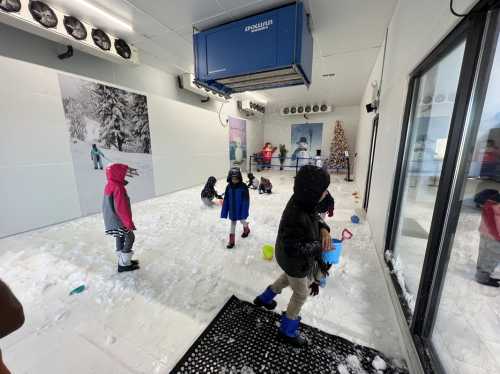 Children playing in a snowy indoor environment, wearing winter clothes and using shovels and buckets.