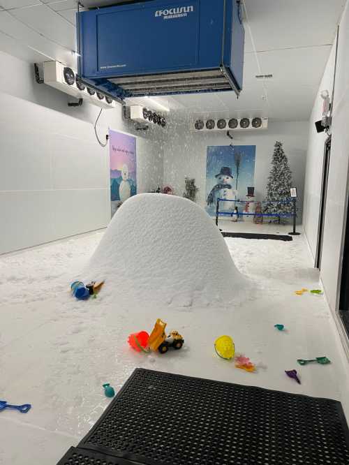 Indoor snowy scene with a large snow mound, scattered toys, and festive decorations in the background.