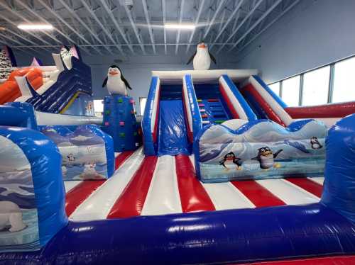 Colorful inflatable playground featuring slides, climbing walls, and penguin decorations in a bright indoor space.