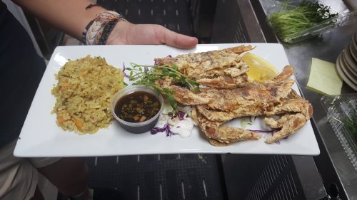 A plate of fried crab with rice, garnished with herbs and a side of dipping sauce, served with a lemon wedge.