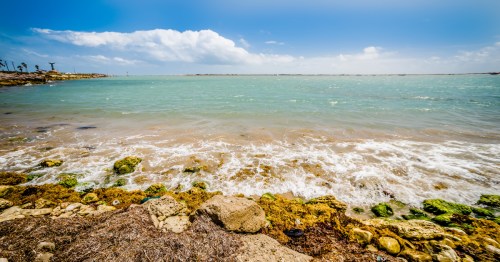 Tropical water rushes over rocks as seen from South Padre Island in Texas with a blue sky overhead