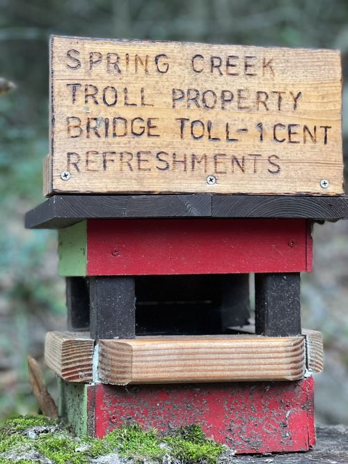 A wooden sign on a small structure reads "Spring Creek Troll Property, Bridge Toll 1 Cent, Refreshments."