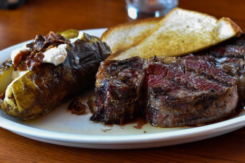 A plate featuring a juicy steak, a baked potato with toppings, and slices of toasted bread.