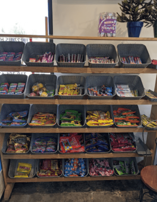 A wooden shelf filled with various colorful candy packages in bins, showcasing a wide selection of sweets.