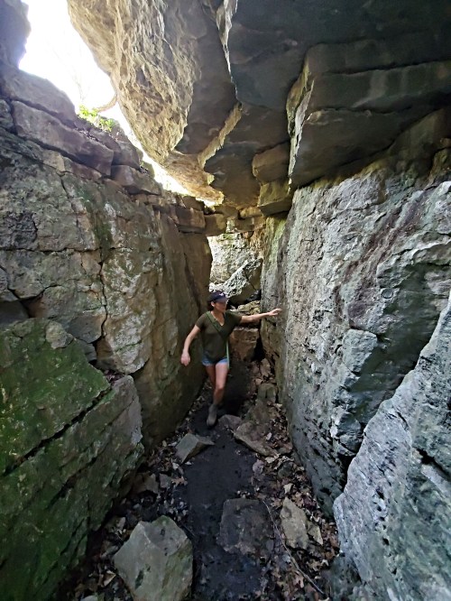 A person navigates through a narrow rocky canyon surrounded by tall stone walls and scattered leaves on the ground.