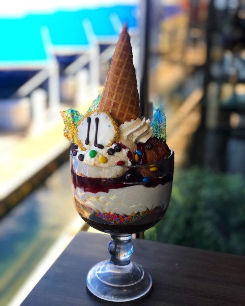 A tall dessert glass filled with layers of ice cream, whipped cream, a waffle cone, and colorful toppings.