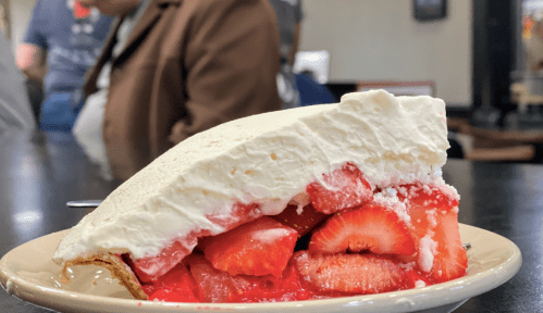 A slice of strawberry pie topped with whipped cream, showcasing fresh strawberries and a red gelatin layer.