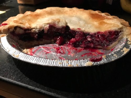 A partially sliced berry pie in a silver pie tin, with a flaky crust and vibrant filling spilling out.