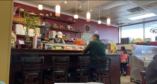 A cozy restaurant interior with a counter, a chef preparing food, and a customer sitting at the bar.