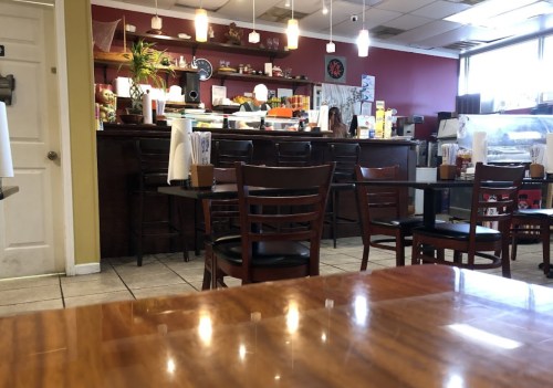 A cozy café interior with empty tables, a counter with food, and a staff member in the background.