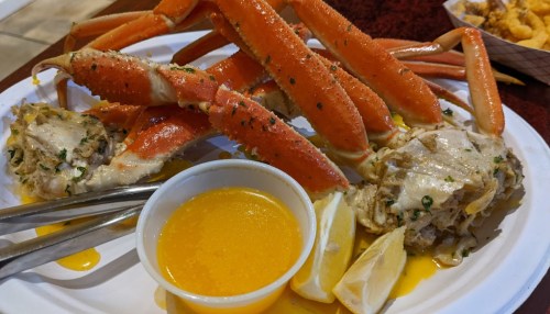 A plate of crab legs with two crab cakes, lemon wedges, and a side of melted butter for dipping.