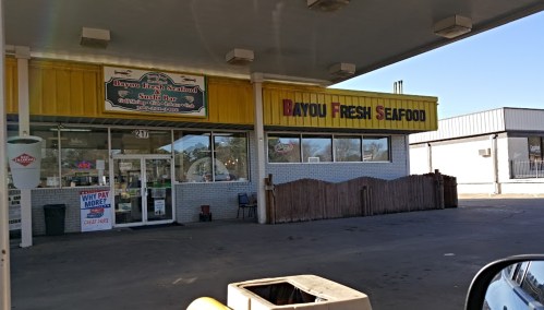 Exterior of Bayou Fresh Seafood, featuring a bright yellow awning and signage, with a parking area in front.