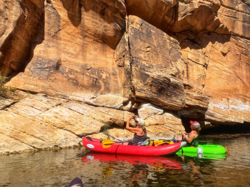 Two kayakers navigate a rocky canyon, one in a red kayak and the other in a green kayak, surrounded by steep cliffs.