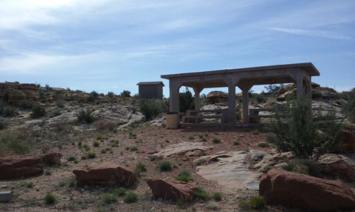 A concrete picnic shelter surrounded by rocky terrain and sparse vegetation under a clear blue sky.