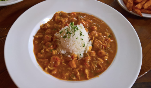 A bowl of flavorful shrimp gumbo with a mound of white rice, garnished with parsley, served on a white plate.