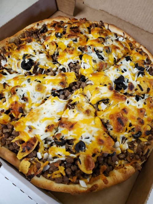 A pizza topped with ground beef, black olives, onions, and melted cheese, served in a cardboard box.