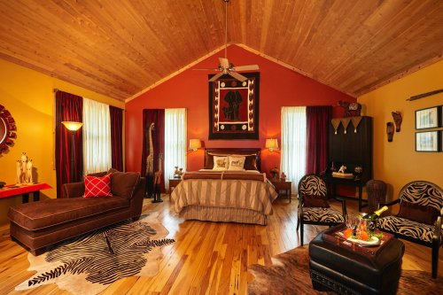 Cozy bedroom with wooden ceiling, colorful walls, a large bed, and stylish decor, featuring animal prints and warm lighting.