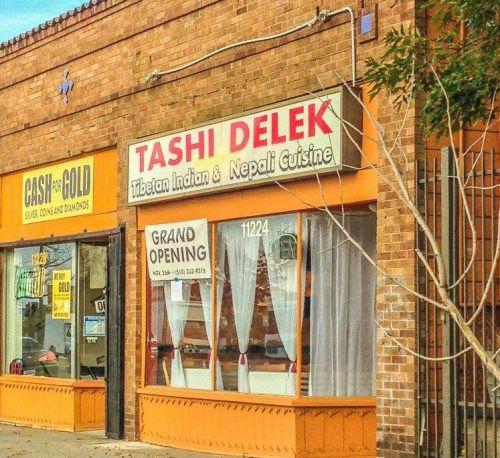 Sign for "Tashi Delek" restaurant featuring Tibetan, Indian, and Nepali cuisine, with a "Grand Opening" banner.