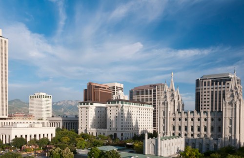 A city skyline featuring modern buildings and a historic temple under a blue sky with scattered clouds.