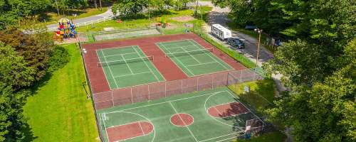 Aerial view of tennis and basketball courts surrounded by trees and a playground in a park setting.