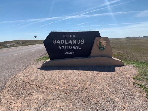 Sign marking the entrance to Badlands National Park, with clear blue skies and grassy landscape in the background.