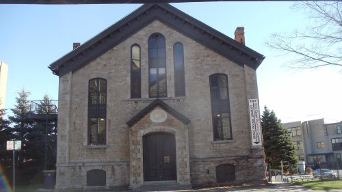 Historic stone building with large windows and a prominent entrance, featuring a sign that reads "Visit."